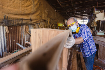 Naklejka na ściany i meble asian senior man carpenter wear protective mask dust and headphone working to measure size of wood. In his own woodworks.