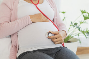 Young asian pregnant woman using stethoscope to listen her belly, during pregnancy as her abdomen...