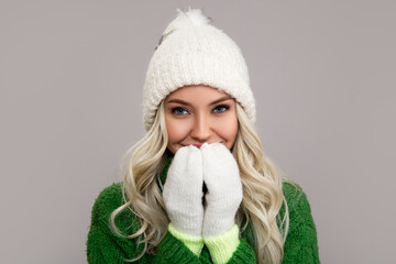 Happy young blonde woman in warm winter clothes smiling closes her mouth with her hands. Snow background