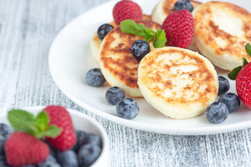 Close up of cottage cheese pancakes with fresh berries on white wooden table. Tasty breakfast food. Syrniki - Image