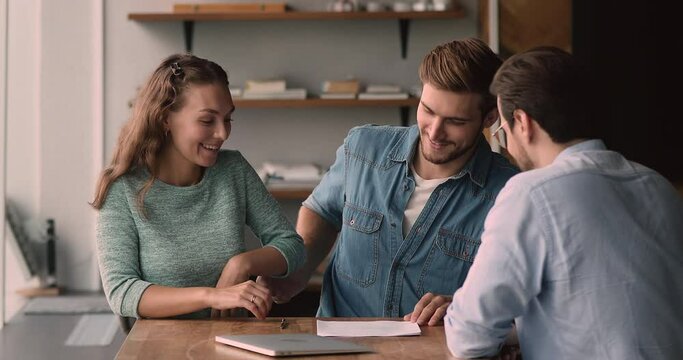 Happy loving family couple discussing apartment purchase with professional real estate agent at office meeting, signing paper contract, getting keys from own accommodation, celebrating successful deal