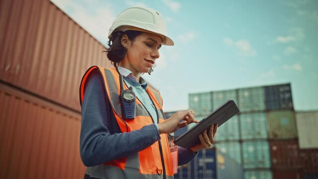 Smiling Portrait of a Beautiful Latin Female Industrial Engineer in White Hard Hat, High-Visibility Vest Working on Tablet Computer. Inspector or Safety Supervisor in Container Terminal.