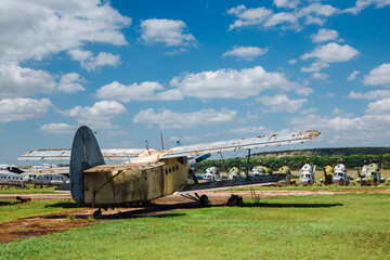 Abandoned, destroyed, rusty old plane stand on the grass under a blue sky with white clouds.