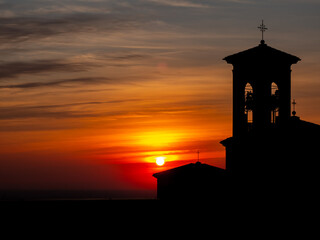 Fiery sunset with a church and bell tower in the foreground. Silhouette of a small bell tower and church roof. Sky with red and orange colors