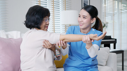 Young senior asia citizen female with scrubs nurse physiotherapy worker at home in rehabilitation therapy service for aging parents. Massage for older care, ache pain joints exercise in old people. - obrazy, fototapety, plakaty