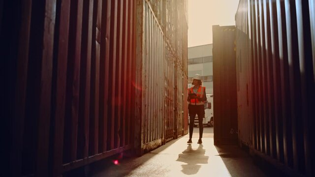 Latin Female Industrial Inspector or Supervisor Wearing White Hard Hat and High-Visibility Vest is Examining the Containers with Her Tablet Computer in a Logistics Shipping Terminal Depot