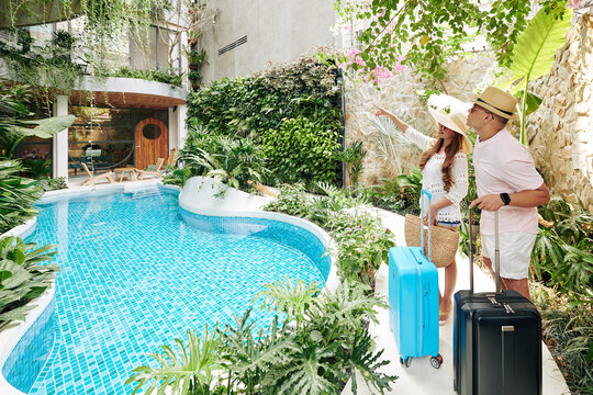 Young Asian Couple With Suitcases Looking At Swimming Pool At Spa Resort