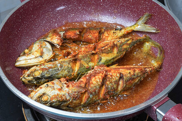 Frying fish with oil using red pan, close up
