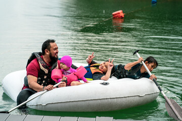 Family wearing life jackets paddling on an inflatable boat in Kenyir Lake, Malaysia.