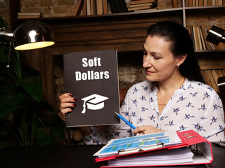 Hand holding black notepad with phrase Soft Dollars . Close-up shot.