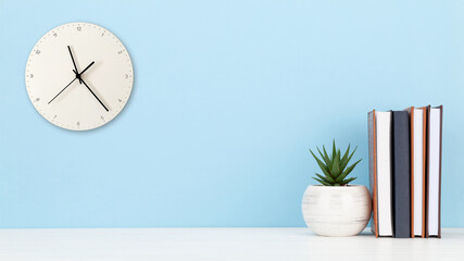 Office desk with wall clock, potted plant and notepads. Work from home