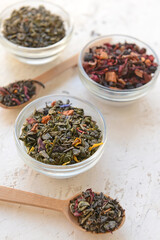 Bowls and spoons with different dry tea leaves on table