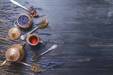 Teapot and spoons with different dry tea leaves on wooden background
