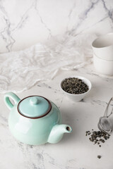 Composition with teapot and dry tea leaves in bowl on light background