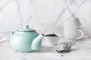 Composition with teapot and dry tea leaves in bowl on light background
