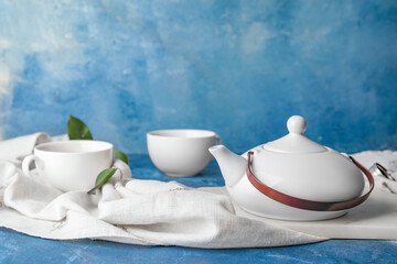 Teapot and cups of tea on color background