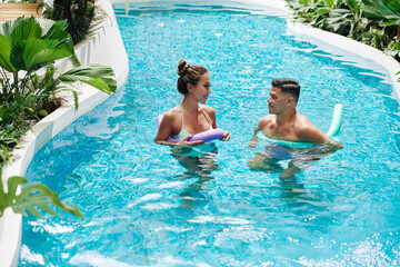 Attractive young Asian woman and her handsome boyfriend lookig at each other when standing swimming...