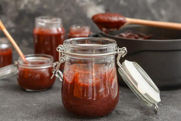 Glass jar with delicious homemade plum jam on dark background