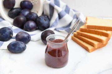 Glass jar with delicious homemade plum jam on light background