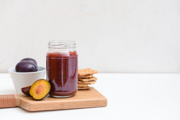 Glass jar with delicious homemade plum jam on light background