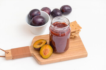 Glass jar with delicious homemade plum jam on white background