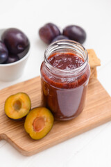 Glass jar with delicious homemade plum jam on white background