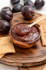 Bowl with delicious homemade plum jam on wooden board