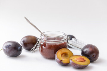 Glass jar with delicious homemade plum jam on white background