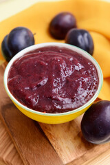 Bowl with delicious homemade plum jam on wooden board