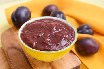 Bowl with delicious homemade plum jam on wooden board
