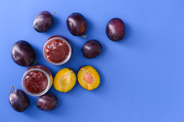 Glass jars with delicious homemade plum jam on color background