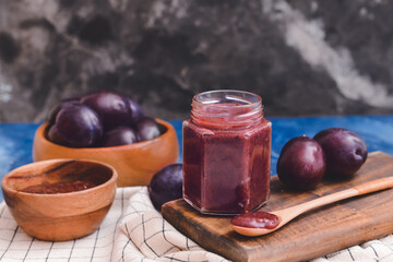 Glass jar with delicious homemade plum jam on color background