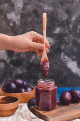 Woman with jar of delicious plum jam on color background