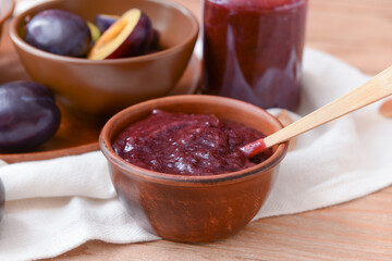 Bowl with delicious homemade plum jam on wooden background