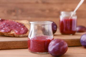 Glass jar with delicious homemade plum jam on wooden background
