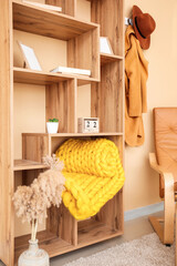 Fototapeta na wymiar Wooden rack with knitted plaid near color wall in room