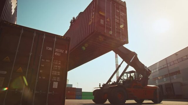 Modern Container Handler Carrying a Large Red Steel Shipping Cargo Storage Container in a Shipyard Terminal. Driver Operating the Handling Equipment is Loading the Crate in the Logistics Center.