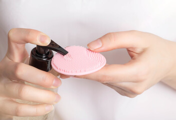 A girl applies a cleansing tonic to a silicone facial brush, close-up. Hygiene and skin care...