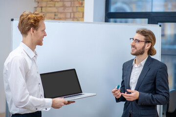 Man in glasses with marker and colleague with laptop