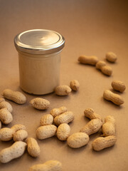 Homemade peanut butter in a glass jar with peanuts in shells scattered around on a craft background in natural light