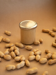 Homemade peanut butter in a glass jar with peanuts in shells scattered around on a craft background...
