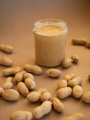 Homemade peanut butter in a glass jar with peanuts in shells scattered around on a craft background in natural light