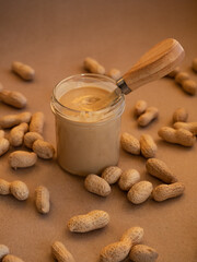 Homemade peanut butter in a glass jar with peanuts in shells scattered around on a craft background in natural light