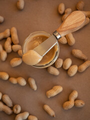 Homemade peanut butter in a glass jar with peanuts in shells scattered around on a craft background...