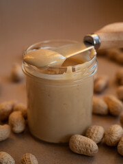 Homemade peanut butter in a glass jar with peanuts in shells scattered around on a craft background in natural light