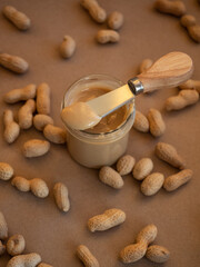Homemade peanut butter in a glass jar with peanuts in shells scattered around on a craft background in natural light