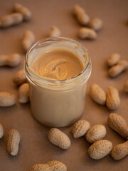Homemade peanut butter in a glass jar with peanuts in shells scattered around on a craft background in natural light