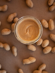 Homemade peanut butter in a glass jar with peanuts in shells scattered around on a craft background in natural light