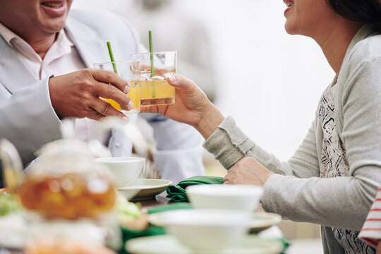 Cropped image of married senior couple toasting with glasses of juice or fruit cocktail when sitting at dinner table