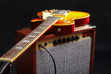 Brown combo amplifier for electric guitar with honey sunburst guitar on black background.